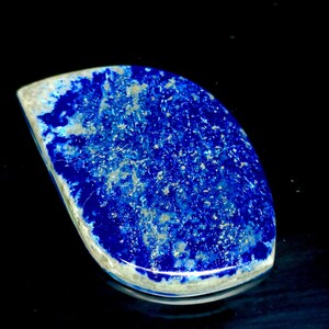 May include: A blue and white cabochon gemstone with a rough, natural texture. The stone has a deep blue color with white veins and flecks throughout.