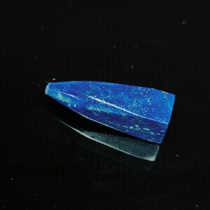 May include: A deep blue, pointed, gemstone with a rough, textured surface. The gemstone is reflecting light, showing a slight shimmer.