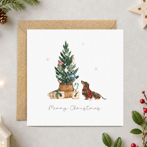 May include: A square greeting card featuring a watercolor illustration of a dachshund wearing a red scarf, sitting beside a decorated Christmas tree in a woven basket with wrapped gifts. The text Merry Christmas is printed below.