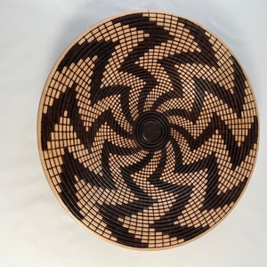 May include: A round, woven wall hanging with a spiral pattern in black and natural wood tones.