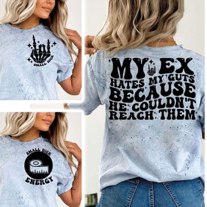 May include: Two light blue t-shirts with black text and graphics. The first shirt has a skeleton hand making a rock and roll sign with the text "Small Dick". The second shirt has the text "My Ex Hates My Guts Because He Couldn't Reach Them".