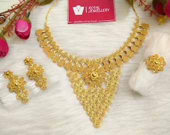 May include: A gold necklace, earrings, and ring set. The necklace features a large, intricate floral design with a triangular shape. The earrings are small and round, and the ring is a simple band with a small flower design. The jewelry is displayed on a white background with a red and white business card that says "Royal Jewellery - jewellery at its finest".