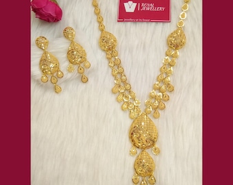 May include: A gold necklace and earrings set with a teardrop design. The necklace has multiple strands of teardrop-shaped links and a large teardrop pendant with intricate detailing. The earrings are also teardrop-shaped with smaller teardrop accents.