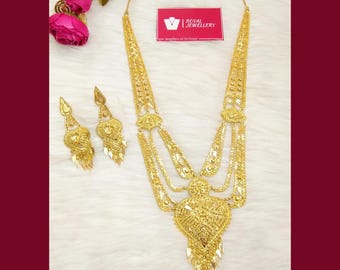 May include: A gold-toned necklace and matching earring set featuring intricate filigree patterns and a large heart-shaped pendant. The necklace includes multiple draped chains. A small rectangular tag displays the text Royal Jewellery.