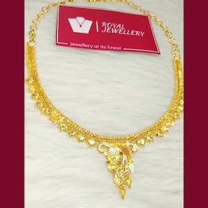 May include: A gold chain necklace featuring a central ornate pendant with intricate filigree details and small dangling elements. The necklace is displayed with a red rectangular tag that reads Royal Jewellery in white text.