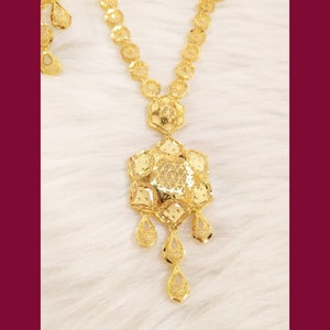 May include: A gold necklace with a large, intricate pendant and matching earrings. The pendant is a geometric design with a filigree pattern. The necklace is made of small, round links.