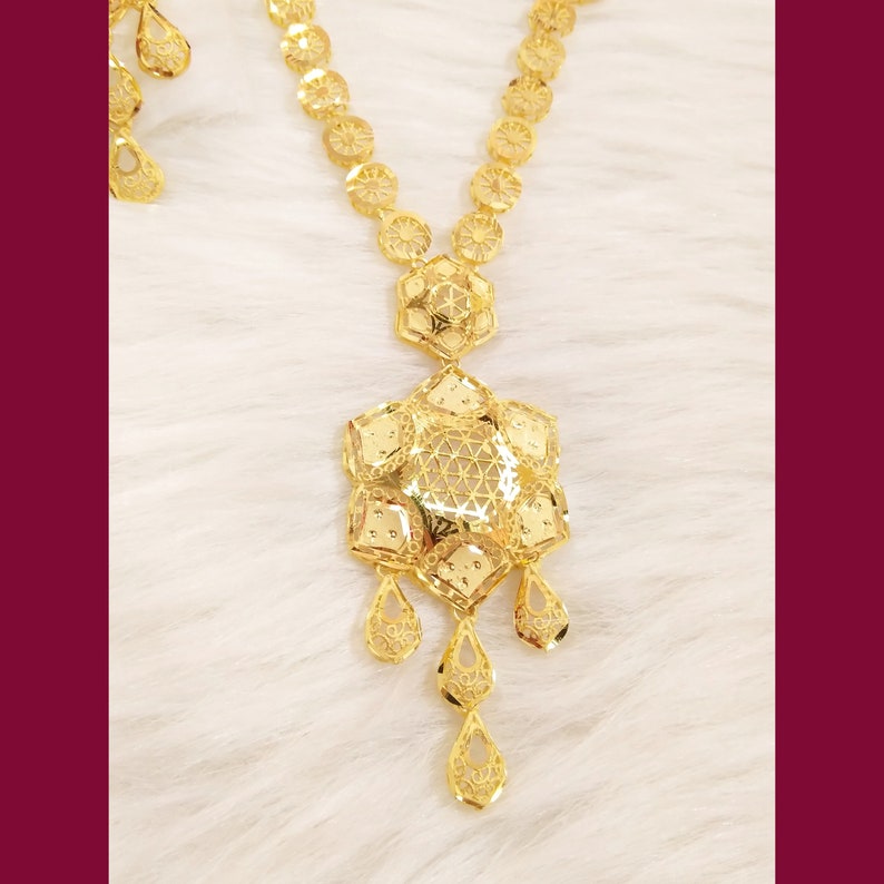 May include: A gold necklace with a large, intricate pendant and matching earrings. The pendant is a geometric design with a filigree pattern. The necklace is made of small, round links.