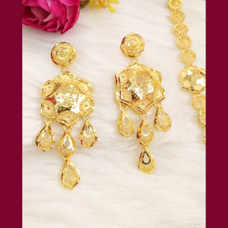 May include: A set of gold earrings with a delicate, intricate design. The earrings feature a large, octagonal pendant with a smaller, teardrop-shaped pendant hanging from it. The earrings are made of gold and have a polished finish.