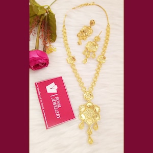 May include: A gold-tone necklace and earrings set with a floral design. The necklace has a long pendant with a large, ornate flower design. The earrings are small and feature a single flower design.