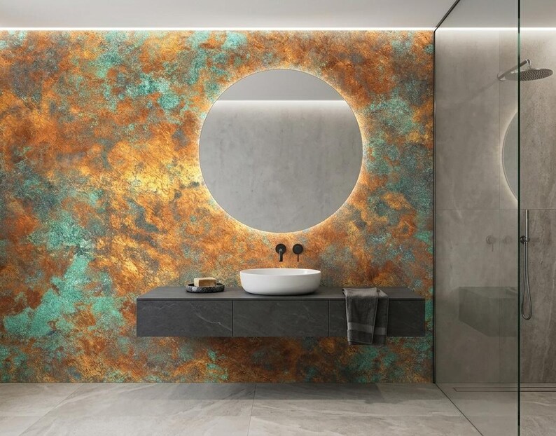 May include: Modern bathroom design featuring a large round mirror with a backlit frame. The wall behind the mirror has a textured, multi-colored finish in shades of orange, green, and brown. A floating vanity with a white sink and black fixtures completes the contemporary look.