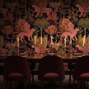 Puede incluir: Un comedor con una mesa de madera oscura y sillas burdeos. El fondo es un papel pintado con motivos de leopardos alados rosas y plantas tropicales. Velas encendidas sobre la mesa crean un ambiente cálido.