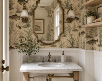May include: A bathroom vanity featuring a white marble countertop, a brass faucet, and a beige towel hanging on a brass bar. Above the sink is an oval mirror with a gold frame, set against wallpaper with a vintage fish and seaweed pattern.
