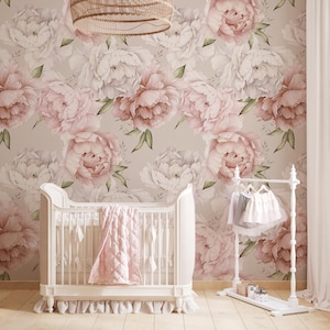 May include: A nursery scene featuring a white crib with a pink blanket, set against a floral peony wallpaper in shades of pink and white. A white clothing rack holds baby clothes. A woven light fixture hangs from the ceiling.