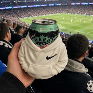 Puede incluir: Una lata de bebida con etiqueta negra y verde claro con el texto Hard Mountain Dew, 5% alcohol y 21+ content, dentro de una sudadera blanca en miniatura con capucha y un logotipo Nike negro en el pecho.