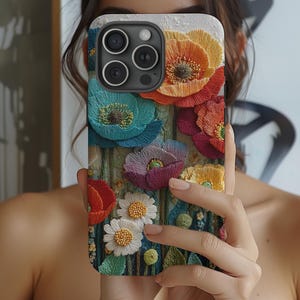May include: A colorful phone case featuring an embroidered floral design. The case showcases a variety of flowers in shades of blue, orange, red, purple, yellow, and white. The case has a textured appearance, with the flowers appearing to be raised from the surface.
