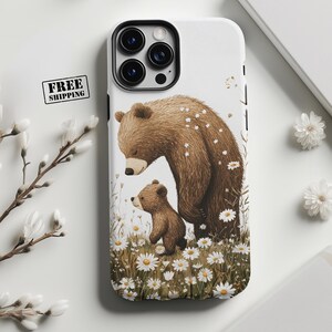 May include: White phone case featuring a brown bear and cub in a field of daisies. The illustration has a whimsical style. The phone case has a black camera lens protector and a black border. The words "FREE SHIPPING" are in a black box.
