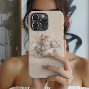 May include: A beige phone case featuring a watercolor illustration of a kitten in a teacup surrounded by flowers. The case has a smooth finish and a camera cutout. The design is soft and pastel-colored.