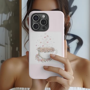 May include: A pale pink phone case with a floral coffee cup illustration. The cup is white, adorned with flowers, and steam rises with heart shapes. The case has a glossy finish and is designed for a smartphone.