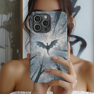 Könnte beinhalten: Handyhülle mit einem Drachendesign, das über einem Winterwald fliegt. Das Kunstwerk verwendet Grau- und Blautöne. Die Hülle hat eine glänzende Oberfläche und einen Kameraausschnitt.