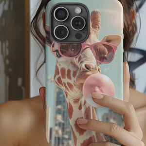 Puede incluir: Funda de teléfono con un diseño de jirafa. La jirafa lleva gafas de sol rosas y sopla una burbuja de chicle. La jirafa tiene un patrón de manchas marrones y blancas. El fondo muestra un paisaje urbano.