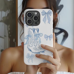 May include: White phone case featuring a blue illustration of cowboy boots with bows and scattered bow graphics. The case has a glossy finish and a camera cutout.