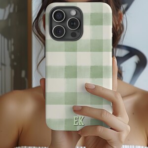 May include: A phone case featuring a green and white gingham pattern. The case has a square design with rounded corners and a camera cutout. The initials "EK" are printed in a light green color at the bottom of the case.