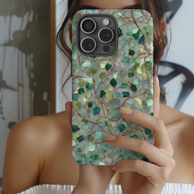 May include: A smartphone case with a nature-inspired design. The case features a mosaic pattern of green and blue leaves and vines against a light background. The case has a camera module with three lenses.