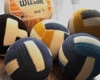 May include: A collection of handmade crochet volleyballs in various colors, including navy blue, black, yellow, and teal, with off-white accents. A Wilson AVP volleyball is also present.