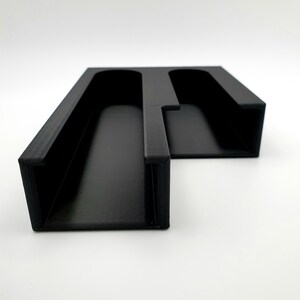 May include: Black plastic organizer with two slots for holding items. The organizer is designed to be mounted on a wall.