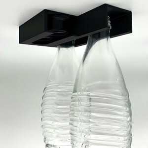 May include: Two clear glass bottles with a textured surface are suspended from a black metal holder. The bottles are empty and appear to be for beverages.