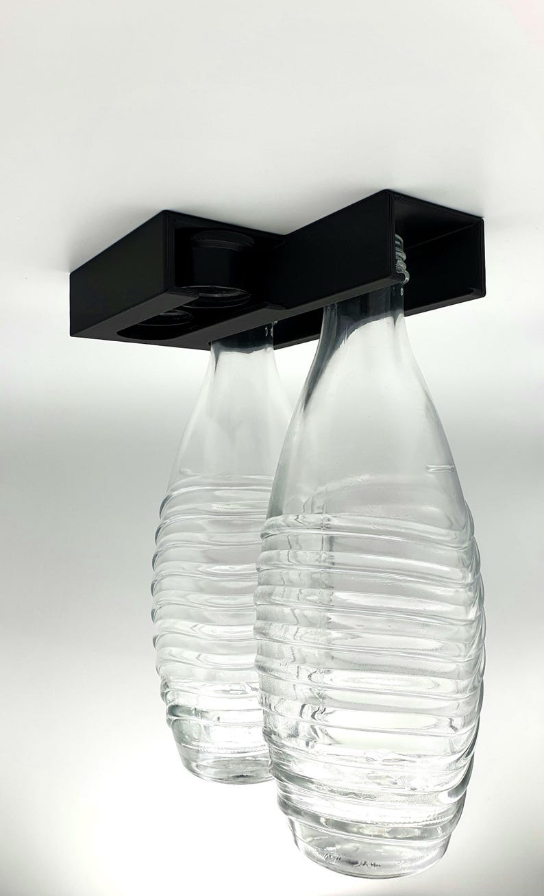 May include: Two clear glass bottles with a textured surface are suspended from a black metal holder. The bottles are empty and appear to be for beverages.