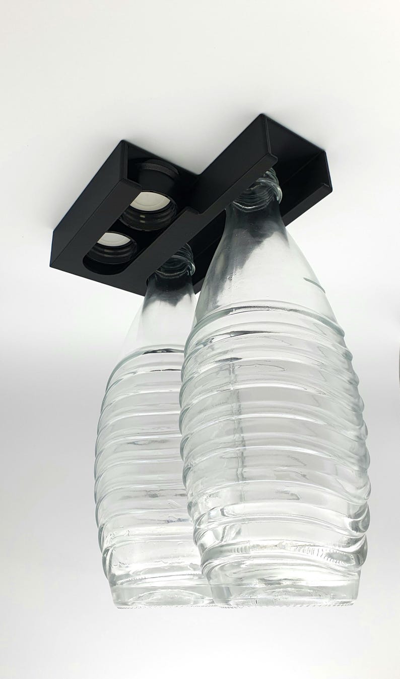 May include: A black metal bottle holder with two clear glass bottles hanging upside down. The bottles have a textured surface.