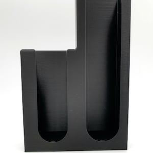 May include: Black plastic organizer with three slots for holding items like pens, pencils, or paintbrushes.