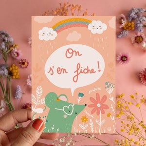 May include: A pink card with a green mouse wearing sunglasses and a speech bubble that says 'On s'en fiche!' The card has a rainbow, clouds, and raindrops. The mouse is in a field of flowers with the words 'inspire' and 'explore' written on the flowers.