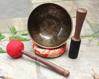May include: A dark brown singing bowl with a red cushion, a wooden mallet with a red felt head, and a wooden mallet with a black felt head.