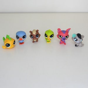 Puede incluir: Una colección de seis pequeñas figuras de animales de plástico. Las figuras son un pez amarillo, un pájaro azul, una ardilla marrón, un loro verde, un gato morado y rojo y un gato gris.