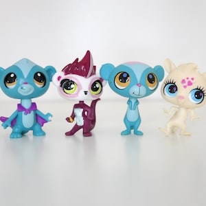 May include: Four colorful, stylized animal figurines. The figures have large eyes and various colors, including blue, purple, and white. The figurines are standing on a white surface.