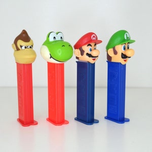 May include: Four different character themed plastic dispensers. The dispensers are red, red, blue, and blue. The characters are Donkey Kong, Yoshi, Mario, and Luigi.