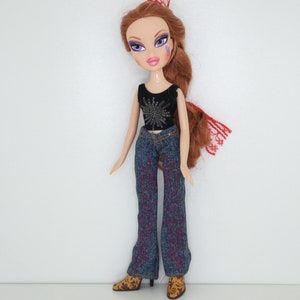 Könnte beinhalten: Eine rothaarige Puppe mit lila Lidschatten und einem schwarzen Tanktop mit silbernem Glitzer. Sie trägt eine blaue Jeans und braune Cowboystiefel.