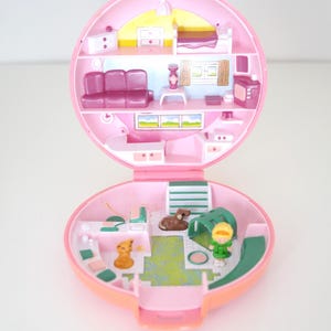 Puede incluir: Una casa de muñecas rosa, abierta y circular, con varios niveles. La casa de muñecas presenta muebles en miniatura, como un sofá, una cama y un televisor. También hay un perro pequeño y una figura. La casa de muñecas está sobre un fondo blanco.