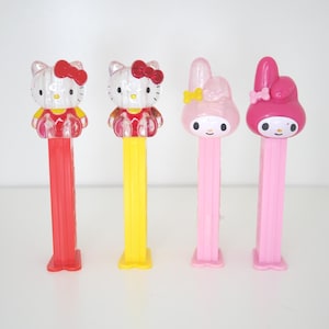 Puede incluir: Cuatro dispensadores de caramelos PEZ coloridos con personajes de dibujos animados populares. Dos dispensadores son Hello Kitty con lazos rojos, y los otros dos son personajes de My Melody. Los dispensadores tienen tallos rojos, amarillos y rosas.
