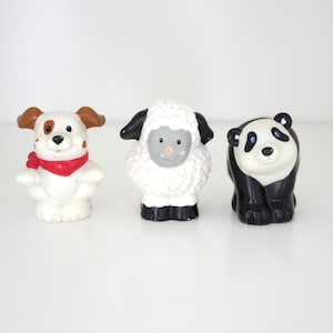 May include: Three colorful toy animal figurines: a white dog with brown ears and a red scarf, a white sheep with black accents, and a black and white panda bear. These figures are designed for children.