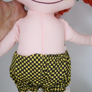 以下が含まれることがあります： ピンク色の体、赤毛、そばかすのハンドメイド人形。 黄色と黒のチェック柄のショートパンツに白いレースのトリムが付いています。 人形の足は緑と赤です。