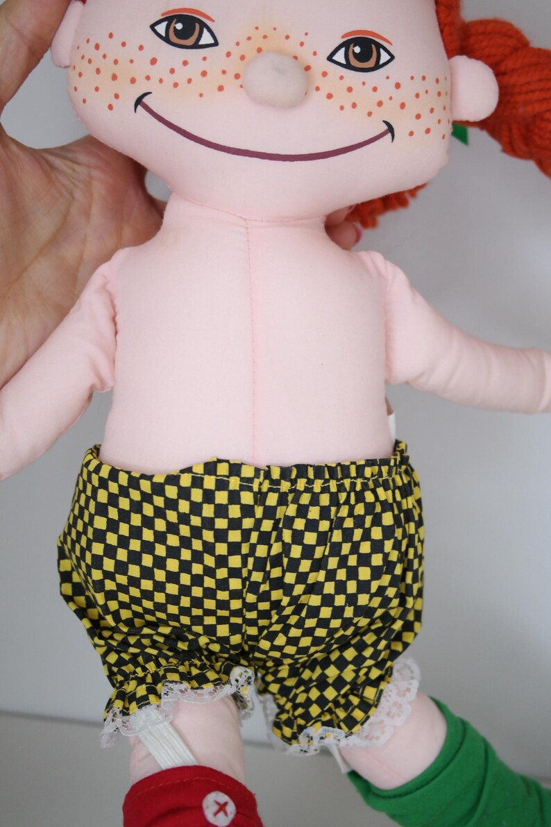 以下が含まれることがあります： ピンク色の体、赤毛、そばかすのハンドメイド人形。 黄色と黒のチェック柄のショートパンツに白いレースのトリムが付いています。 人形の足は緑と赤です。