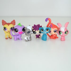 Puede incluir: Una colección de siete animales de juguete de plástico de colores. Los animales incluyen una mofeta, un mono, un erizo, un animal morado con una hoja verde en la cabeza, un animal rosa con pelaje blanco, un animal azul con una cola larga y un animal amarillo y naranja con orejas grandes.