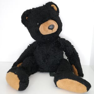 May include: A black plush teddy bear with tan accents on the snout, ears, and feet. The bear is sitting with its arms and legs spread out. The bear has a dark brown nose and a friendly expression.