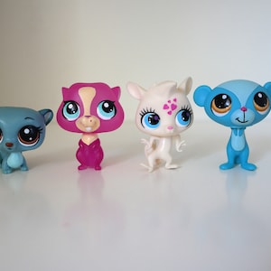 May include: Four small plastic toy animals with large eyes. The animals are a blue and gray squirrel, a pink and purple squirrel, a white and pink kangaroo, and a blue and yellow lemur.