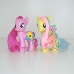 May include: Two My Little Pony toys, one pink with a blue balloon and the other yellow with a rainbow mane and wings.