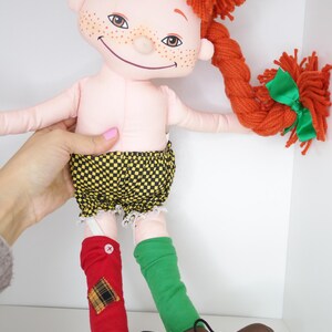 以下が含まれることがあります： 赤い糸の髪を三つ編みにし、緑のリボンをつけた手作りの人形。そばかすのある顔で、黄と黒のチェック柄のショートパンツ、赤と緑の靴下、茶色の靴を履いています。ユニークで気まぐれな玩具。