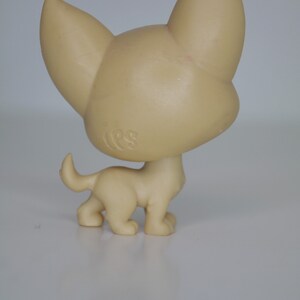 May include: A small, beige plastic toy dog with floppy ears and a short tail. The dog is standing on all four legs and has a small, round head.